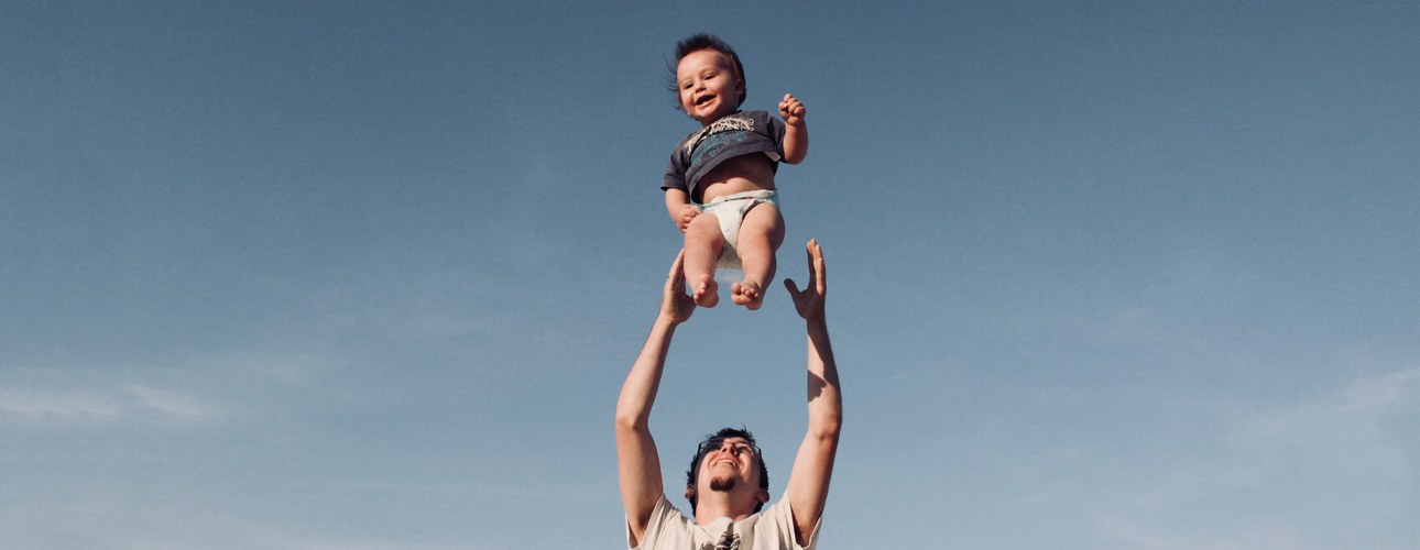 Kopfbild mit Mann der ein lachendes Baby hochwirft und auffängt
