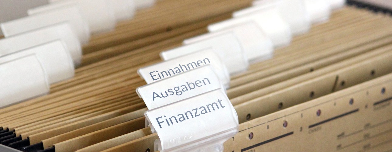 Kopfbild mit Akten zum Thema Einnahmen, Ausgaben und Finanzamt